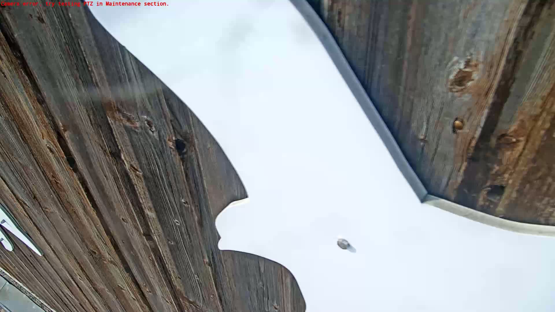 A large white, bat-shaped object is mounted against a dark brown wooden wall outdoors on a partly cloudy day.