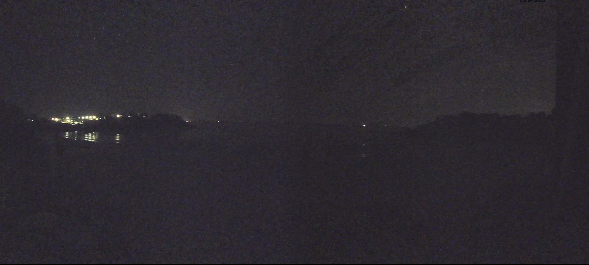 A dark, nighttime view of a body of water reflecting a few distant lights under a clear, starry sky.