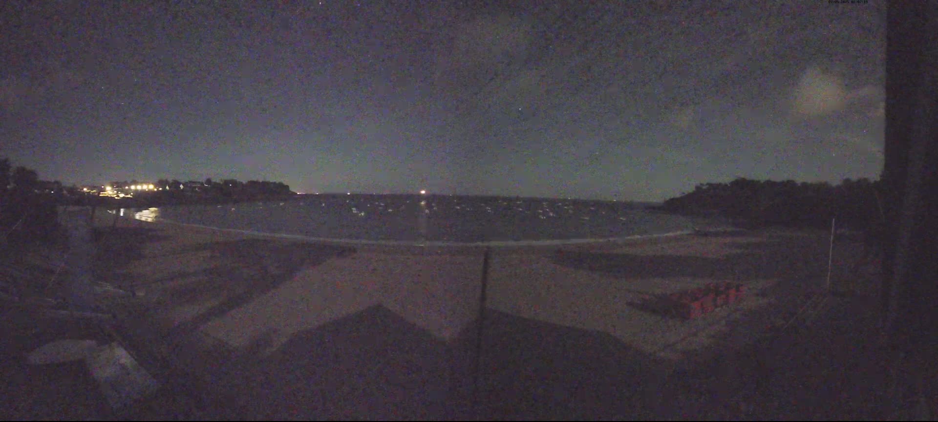 A nighttime view shows a dark sandy beach with calm water under a mostly clear, dark sky.