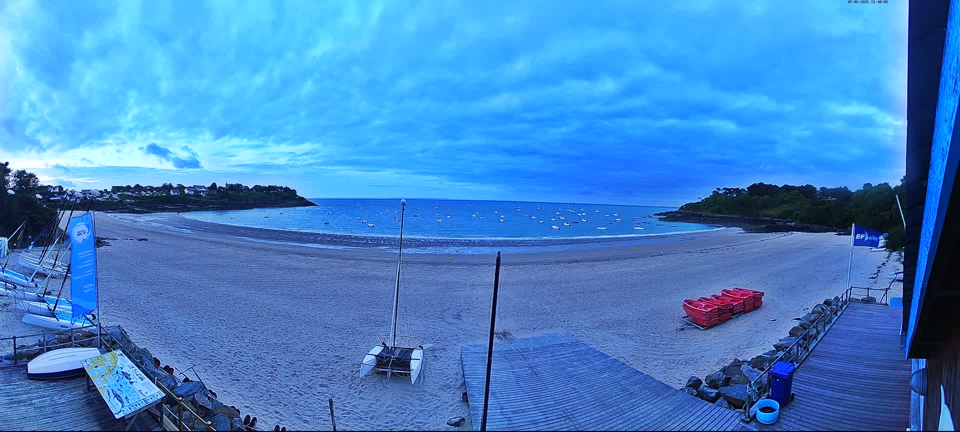A sandy beach with calm water and numerous small boats is visible under a mostly cloudy, blue sky.