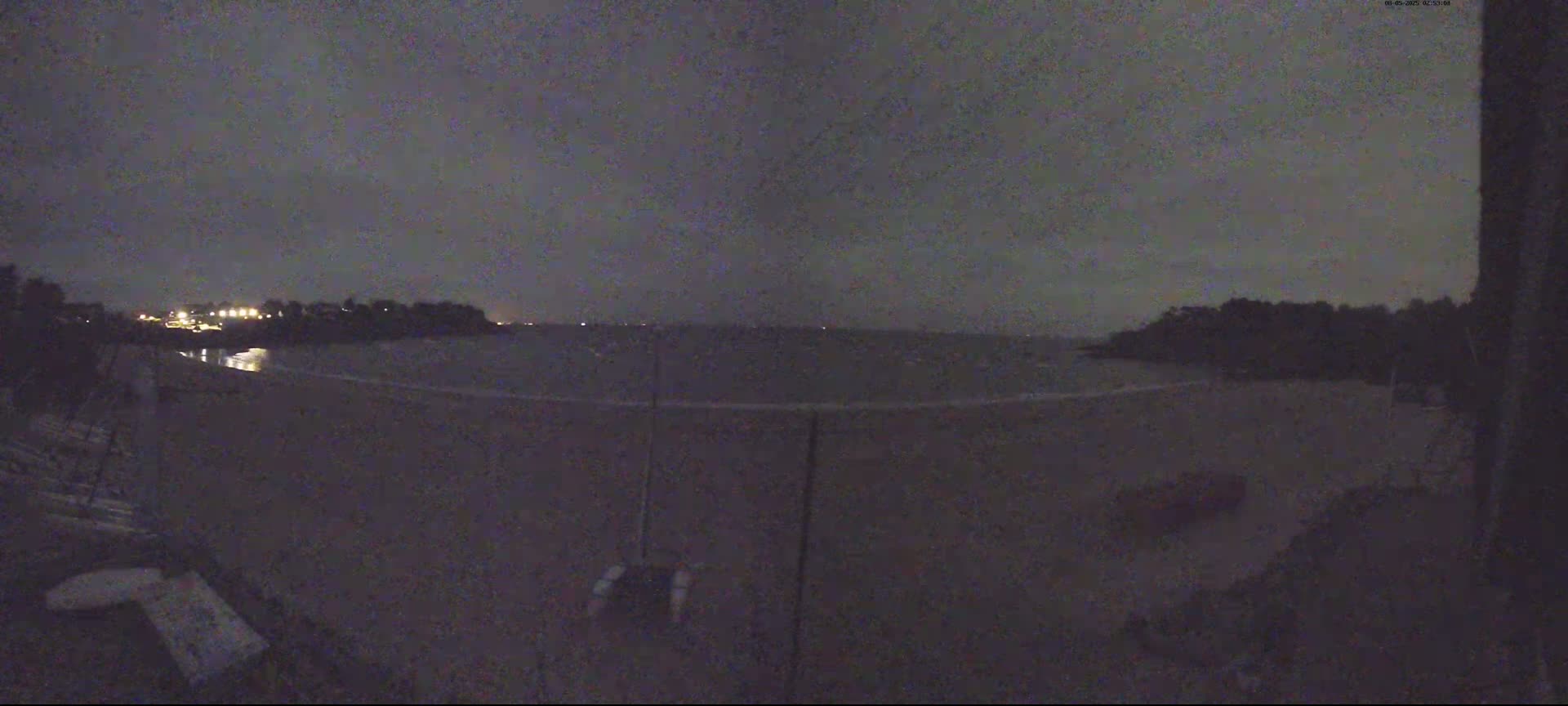 A dark, nighttime view of a beach and calm water under a cloudy sky.