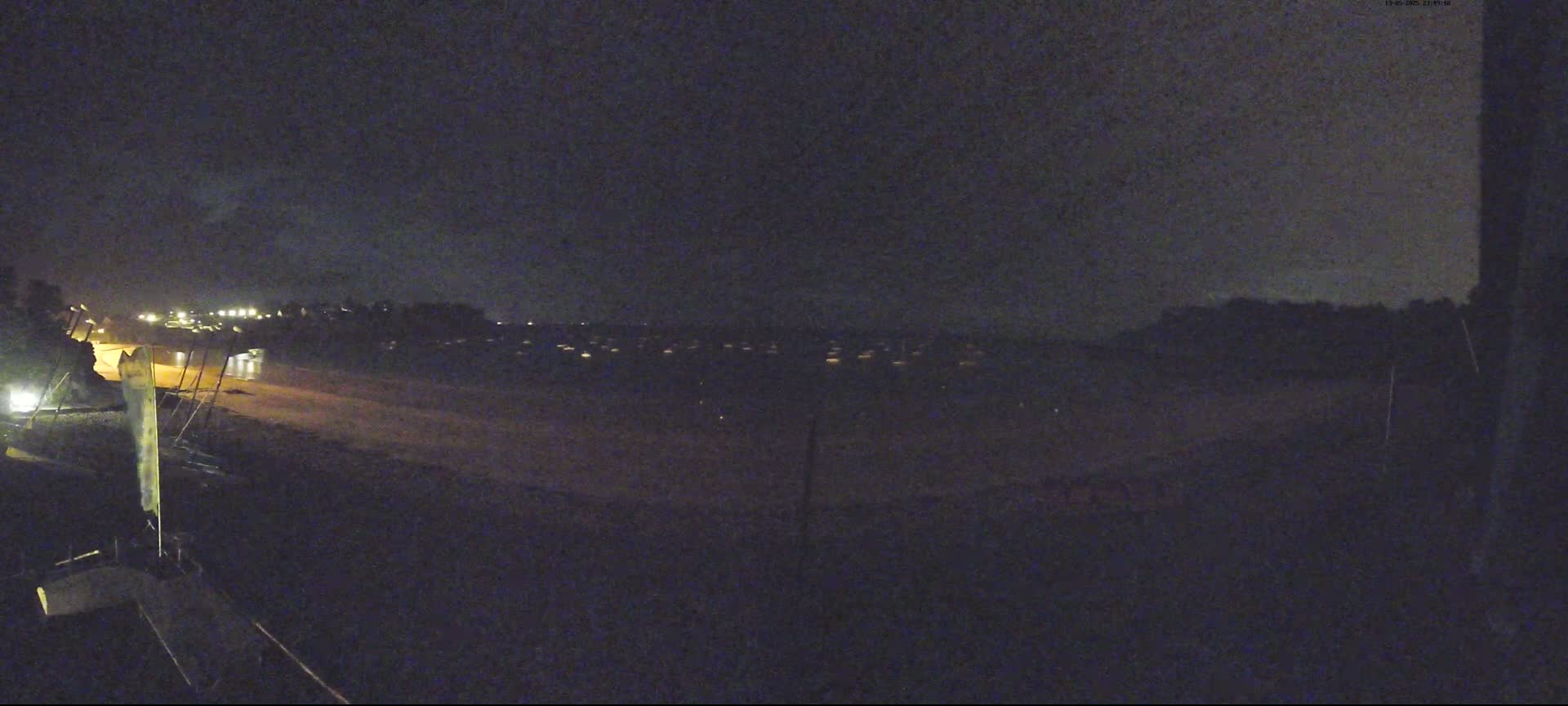 A nighttime view of a dark beach with faintly lit buildings in the distance under a cloudy sky.