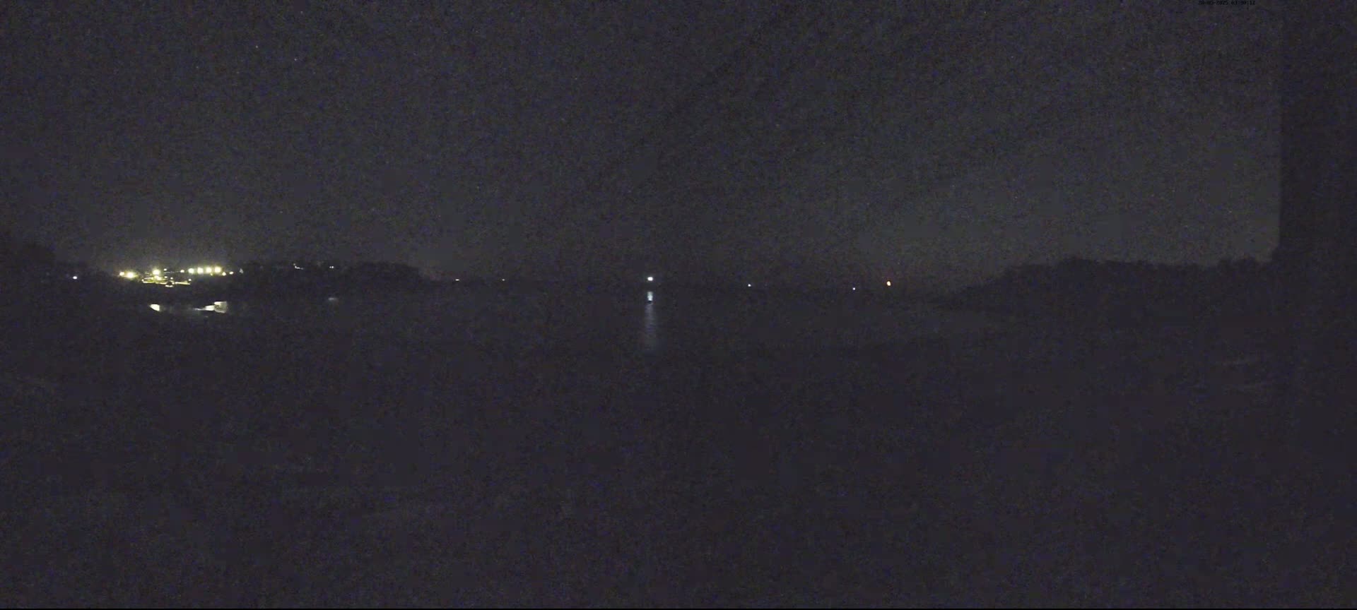 A dark, nighttime scene shows a body of water with faint lights on the far shore and a single light in the water.