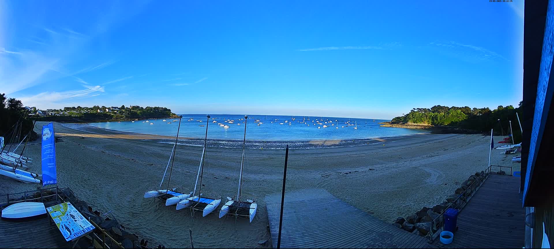 A sandy beach with several sailboats on the shore and many more in the calm, blue water under a clear, bright blue sky.