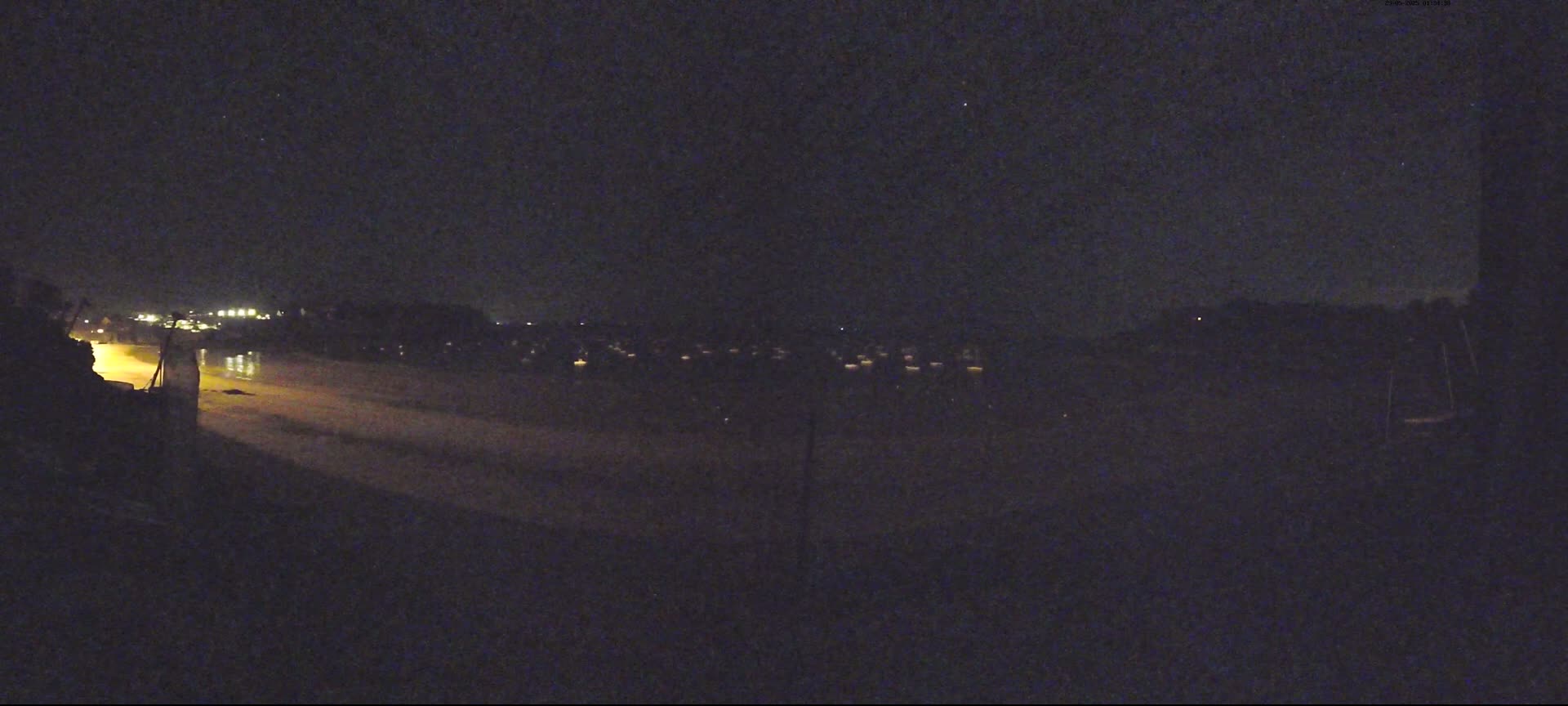 A nighttime view of a dimly lit beach and distant town under a dark, clear sky.