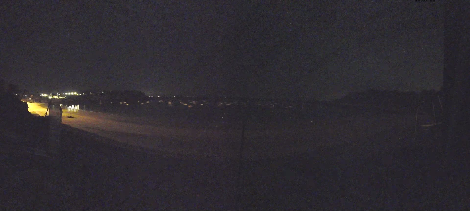 A nighttime view shows a dimly lit shoreline with distant houses and a dark, starlit sky.