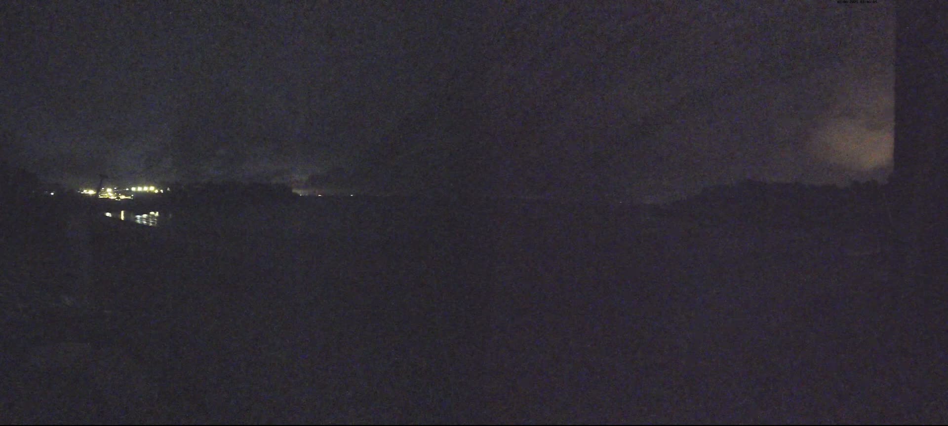 A nighttime view shows a dark landscape with distant, faint lights and a mostly cloudy sky.
