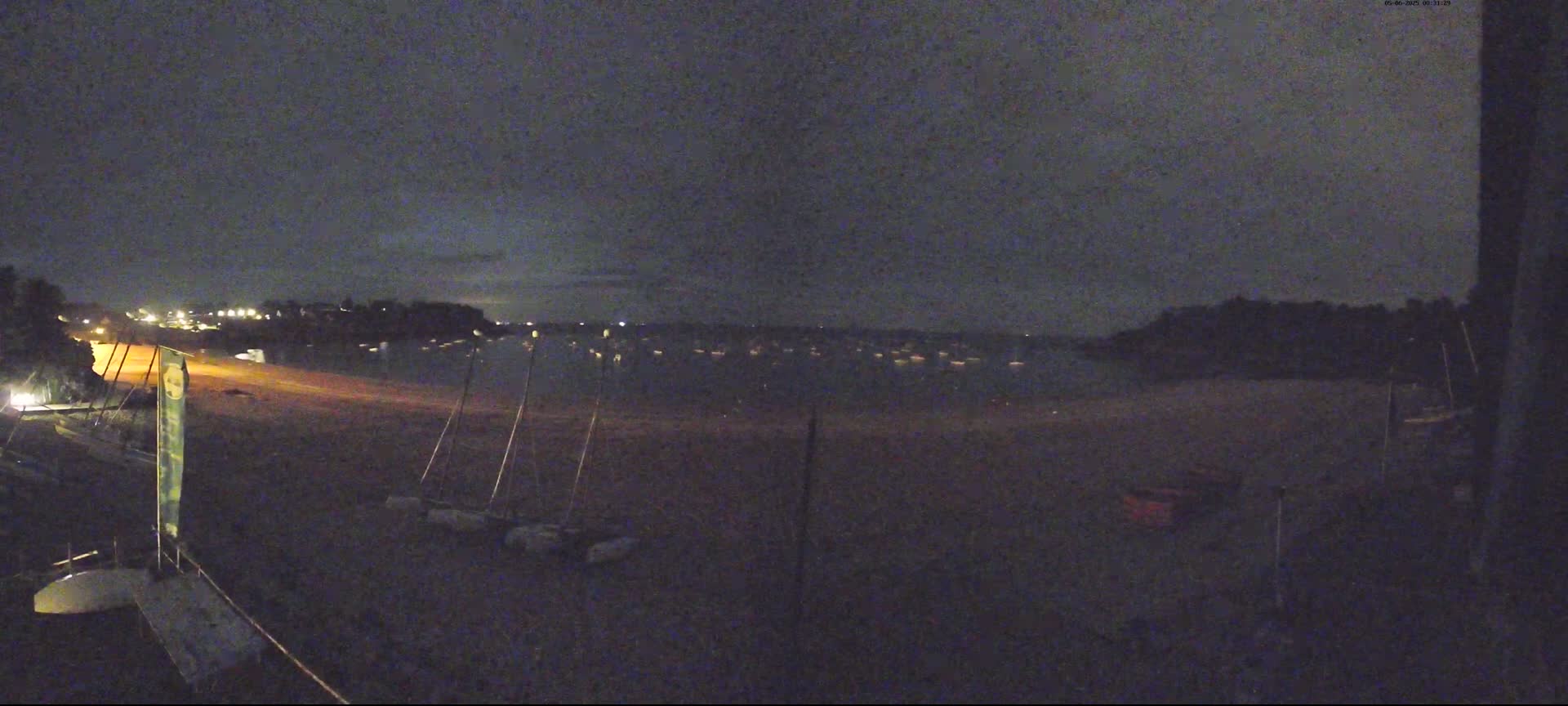 At night, under a dark sky, a sandy beach is shown with several sailboats on the water and others beached on the sand.