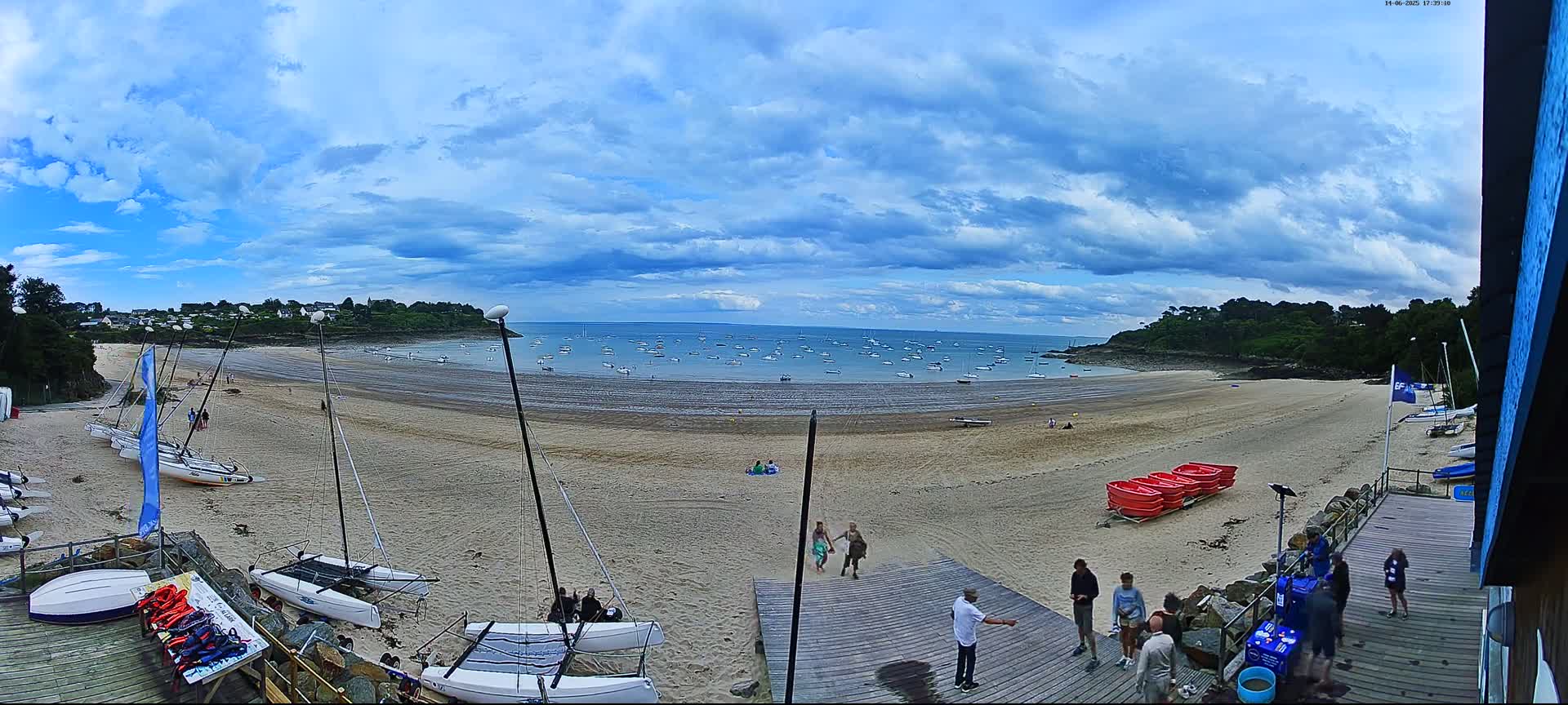 A sandy beach with numerous sailboats and people on a partly cloudy day.