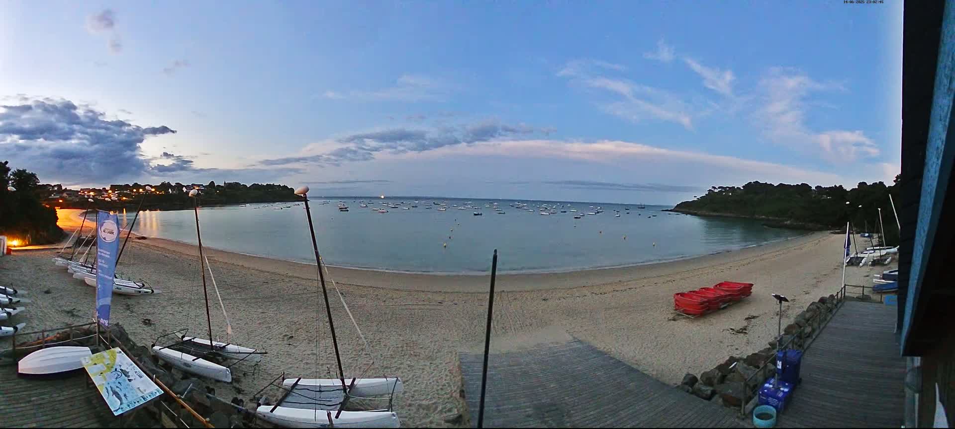 A sandy beach with numerous sailboats and people on a partly cloudy day.