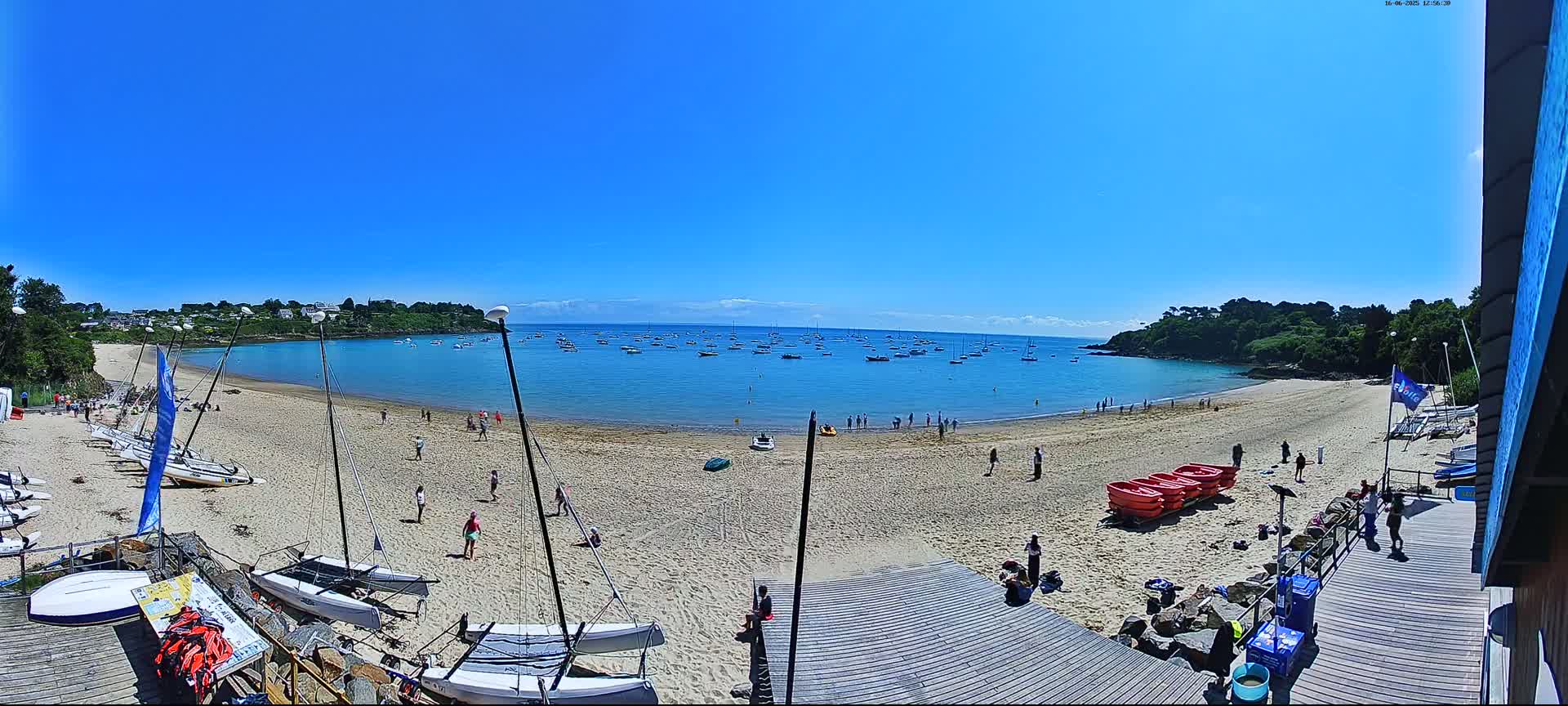 A sandy beach with numerous sailboats in the water and people enjoying a sunny day.