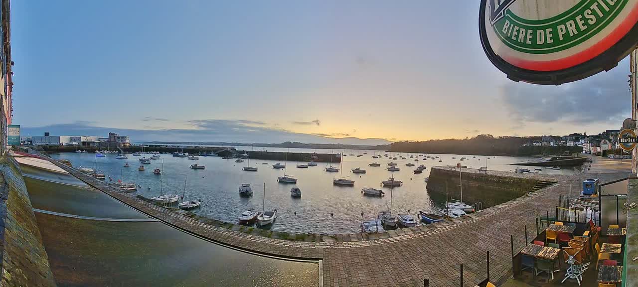 A calm harbor filled with numerous small boats at sunset, under a clear, pale sky.