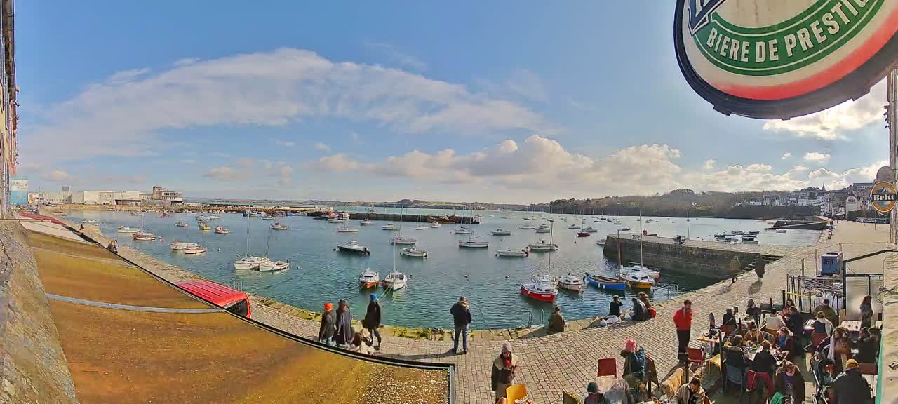 A sunny day reveals a harbor filled with numerous boats and people relaxing outdoors near a waterfront patio.