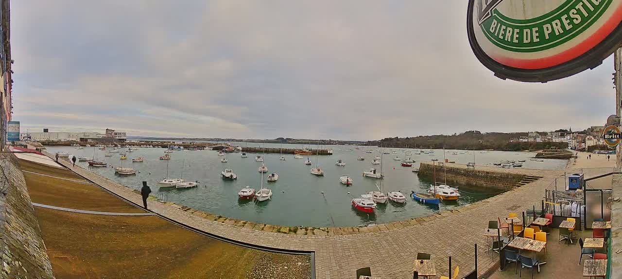 A harbor filled with numerous small boats under a cloudy sky, viewed from an elevated position near an outdoor café.