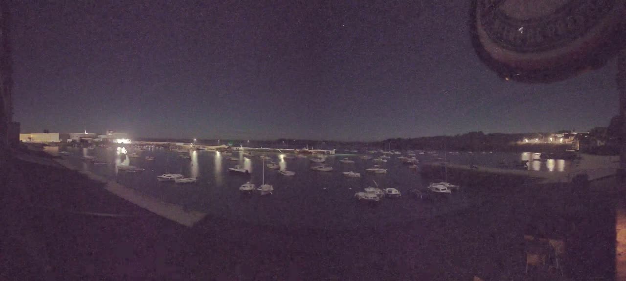 Many small boats are moored in a calm harbor at night under a dark, clear sky.