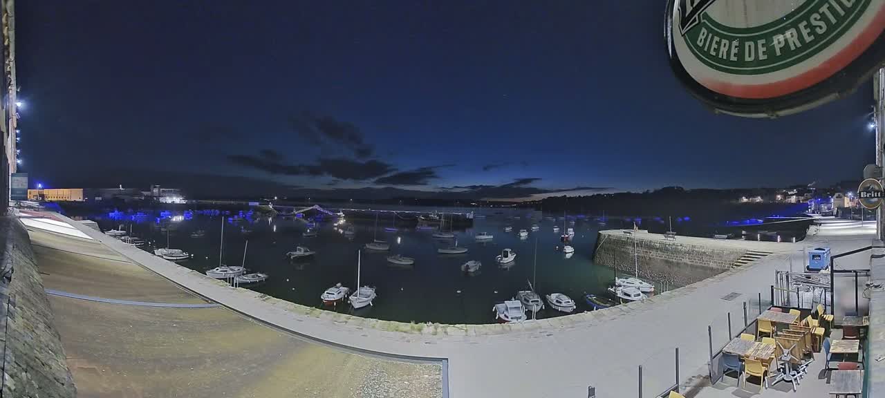 Numerous boats are moored in a calm harbor at night under a dark blue sky.