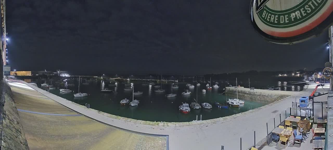 A nighttime view of a harbor filled with boats, under a dark, cloudy sky.