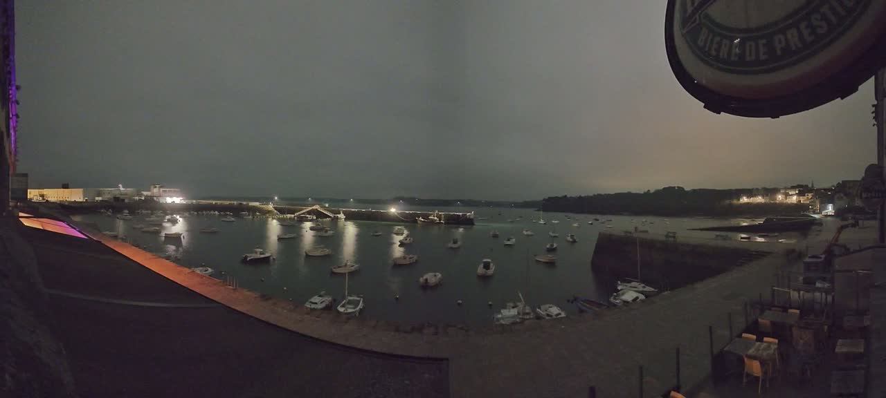 A nighttime view of a harbor filled with numerous boats under a dark, overcast sky.