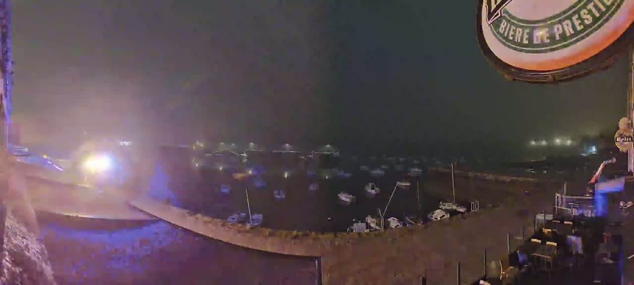 A nighttime view of a harbor filled with boats in foggy conditions, observed from a high vantage point.