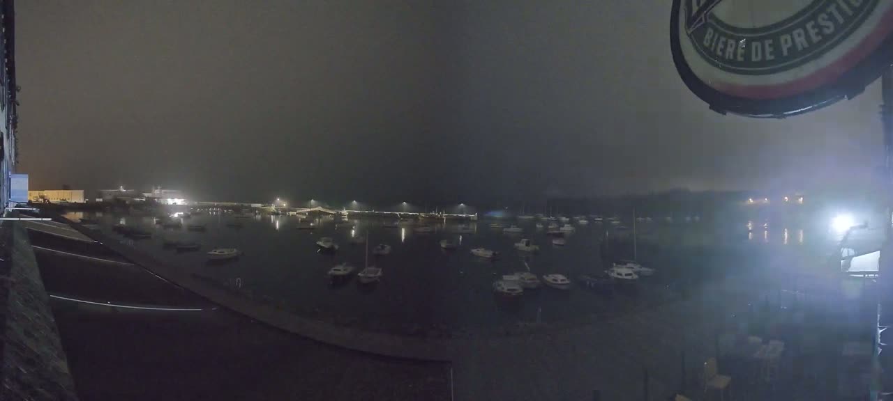 Many small boats are moored in a harbor at night in foggy conditions.