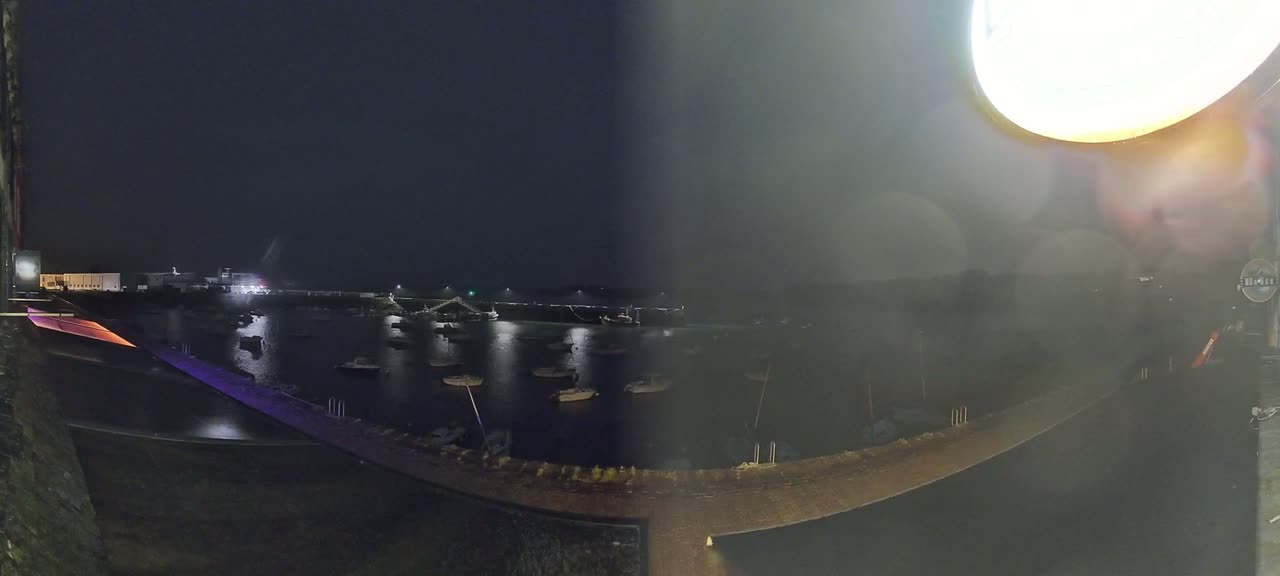 A nighttime view of a harbor filled with boats, illuminated by lights, under a dark sky.