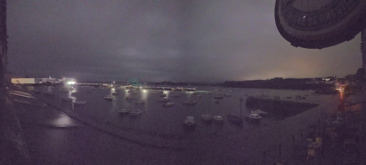 Many boats are moored in a dark harbor under a cloudy night sky.