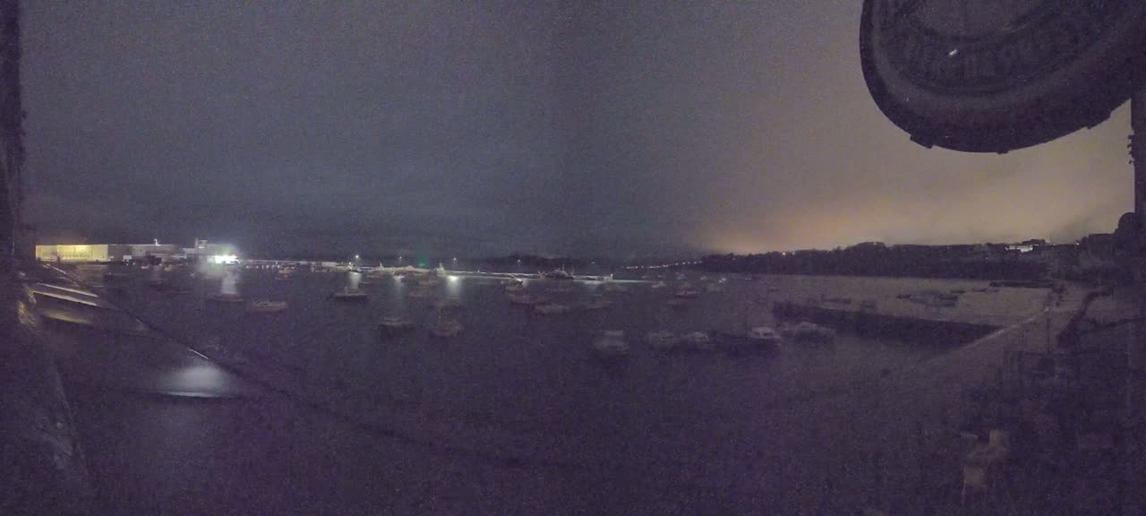 Many boats are moored in a dark harbor at night under a cloudy sky.