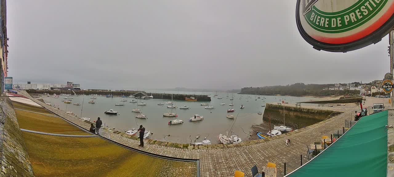 A harbor filled with numerous boats on a cloudy day, viewed from a stone quayside.