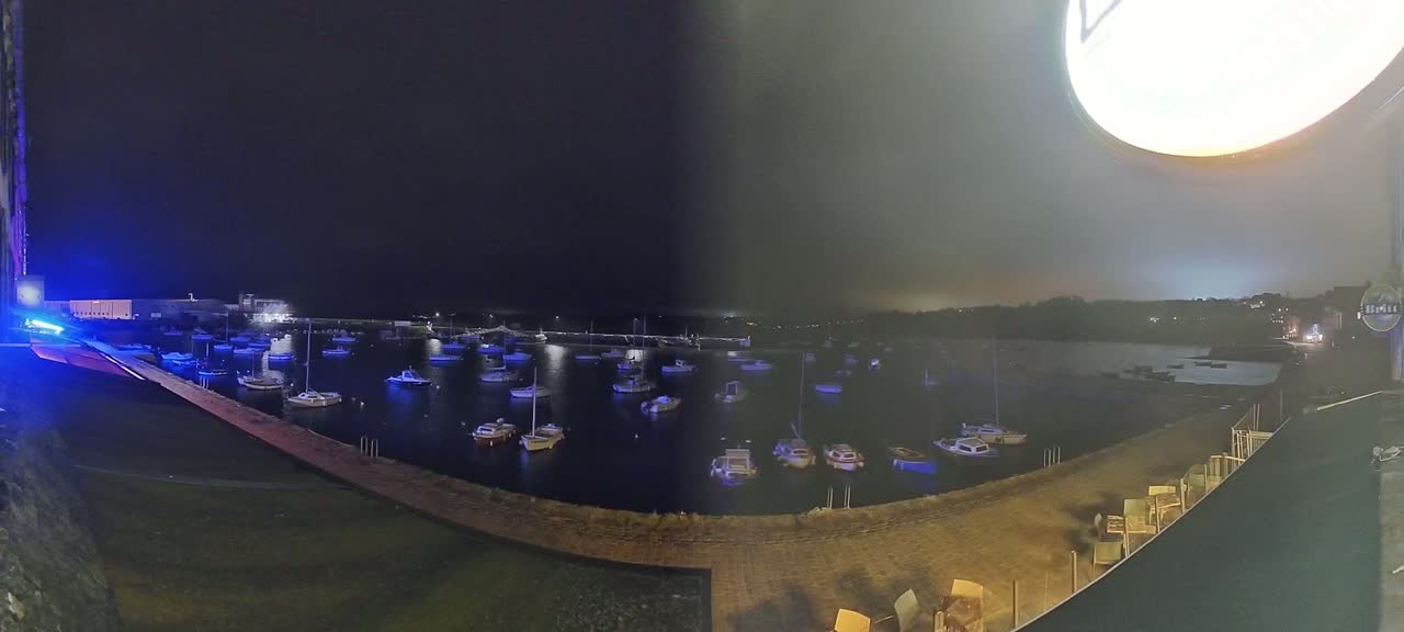 A nighttime view of a harbor filled with numerous boats under a cloudy sky.