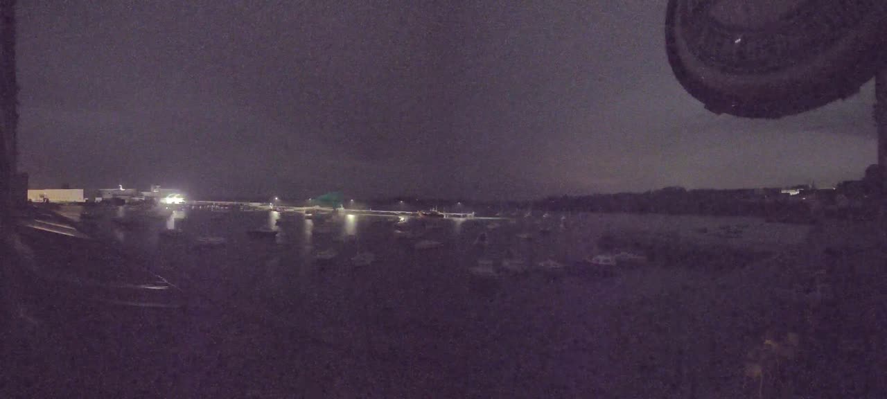 A nighttime view of numerous boats at anchor in calm water, under a dark, cloudy sky.