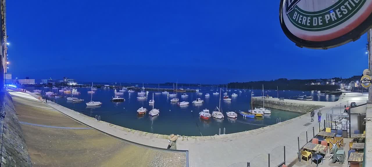 Many small boats are moored in a harbor at twilight under a clear, dark blue sky.