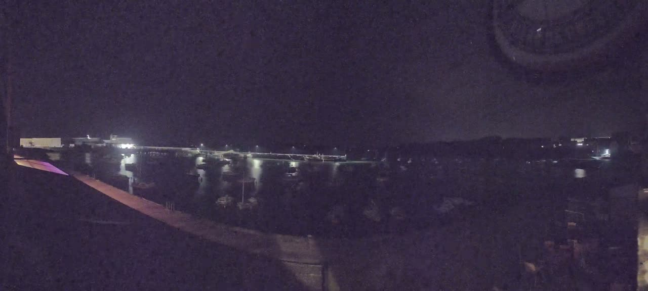 A nighttime view of a harbor filled with numerous boats, illuminated by faint lights under a dark sky.