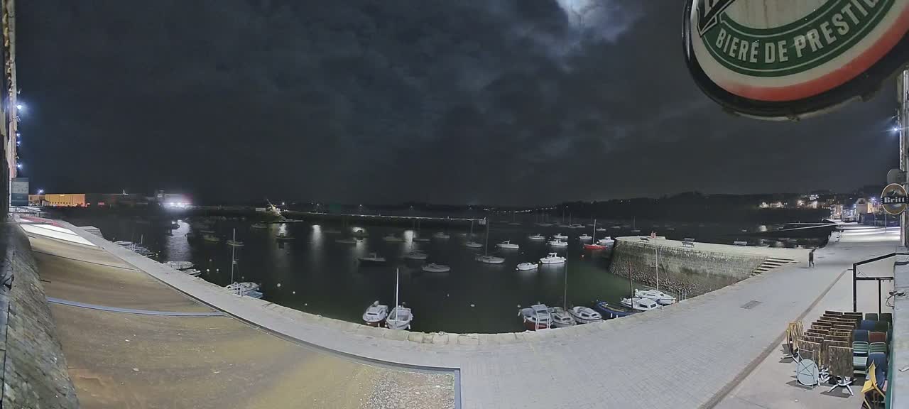 A nighttime view of a harbor filled with numerous small boats under a dark, cloudy sky.