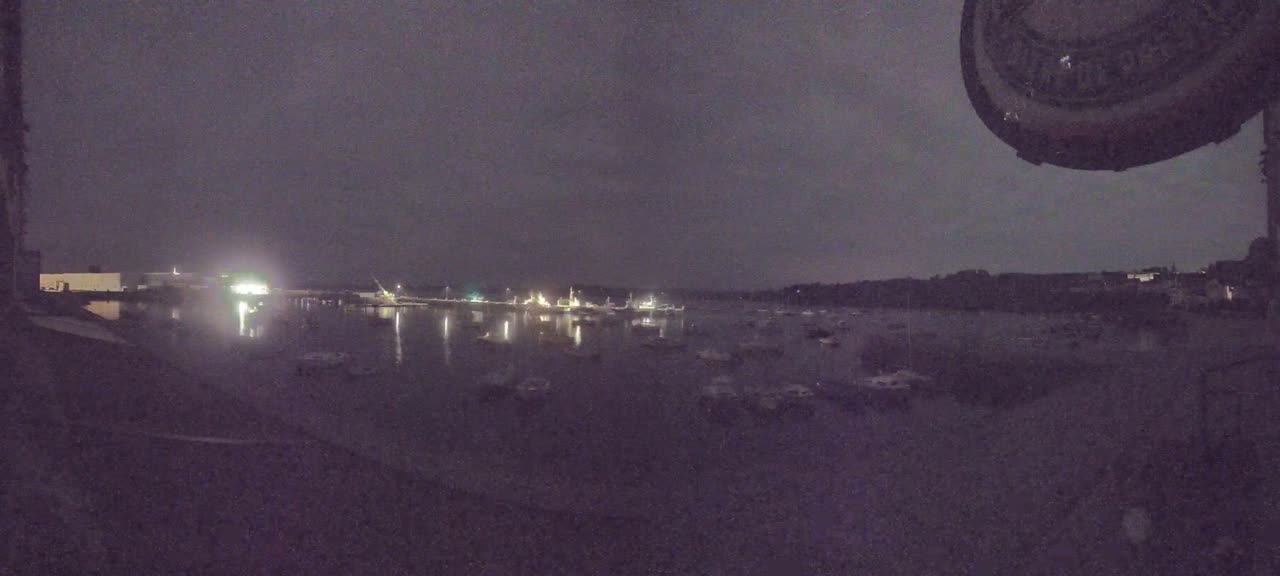 Many boats are moored in a dark harbor at night under a cloudy sky.