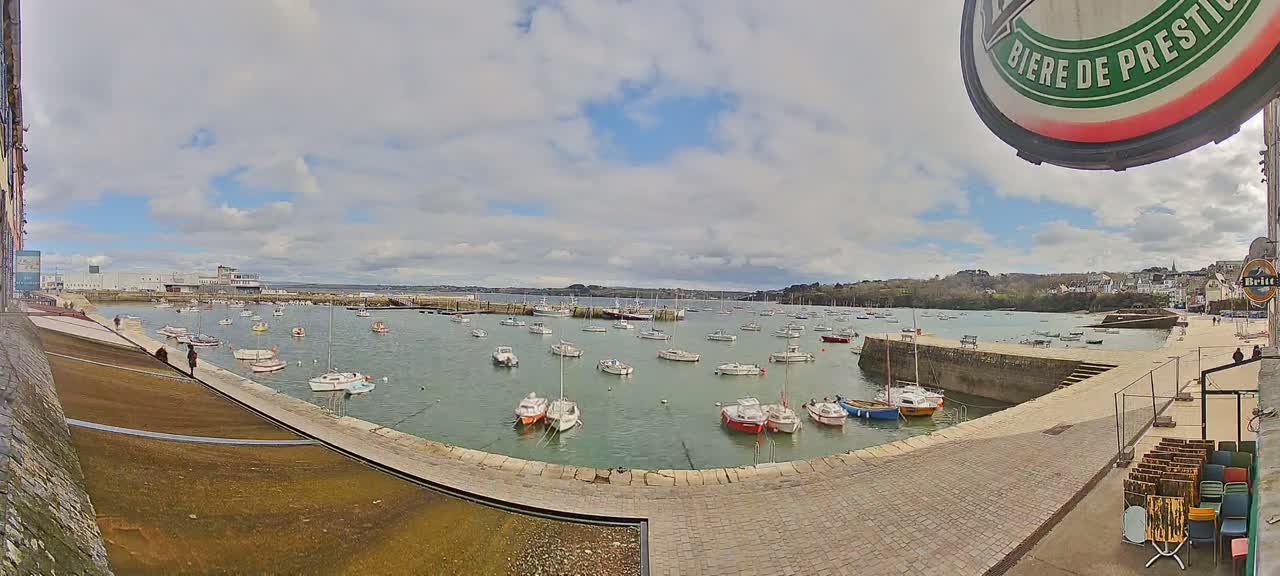 A harbor filled with numerous sailboats and motorboats under a partly cloudy sky.