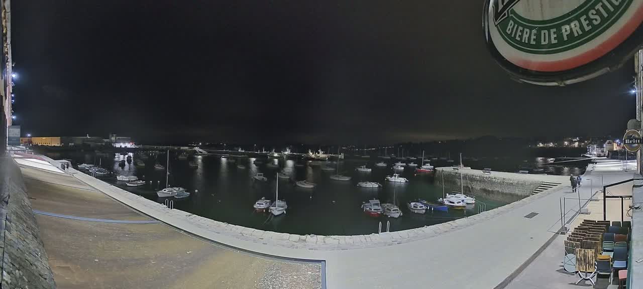 Many boats are moored in a harbor at night under a dark sky.