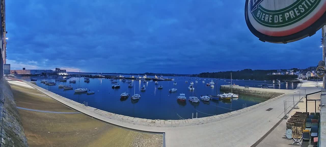A calm harbor filled with numerous small boats at twilight under a mostly clear, dark blue sky.