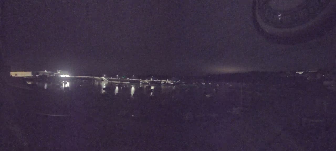 At night, several boats are moored in a harbor under a dark sky.