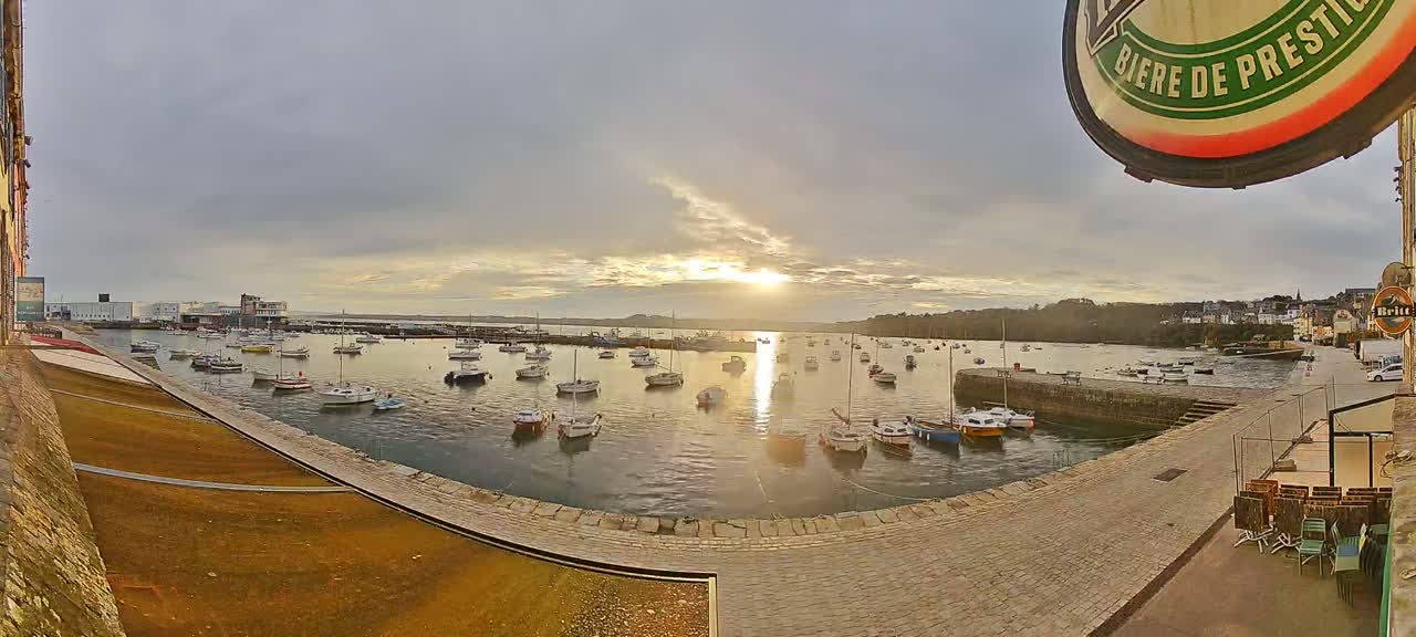 Many small boats are moored in a calm harbor at sunset under a cloudy sky.
