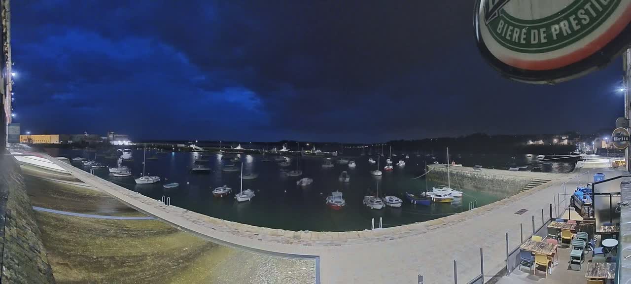 A harbor filled with boats is visible at night under a dark blue, cloudy sky.