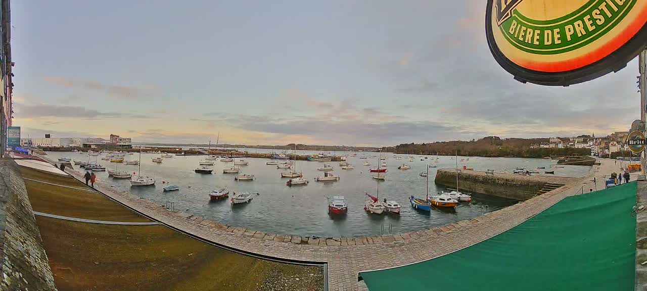 Many small boats are moored in a harbor under a cloudy, twilight sky.