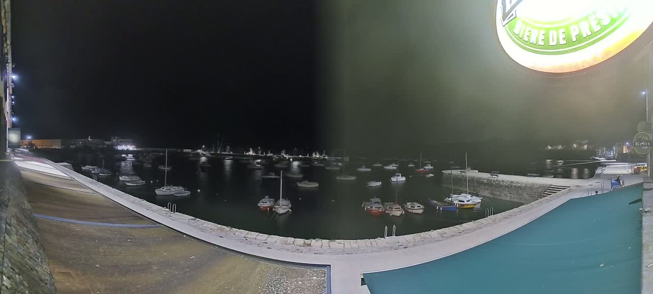 A nighttime view of a harbor filled with numerous boats, under a dark sky.