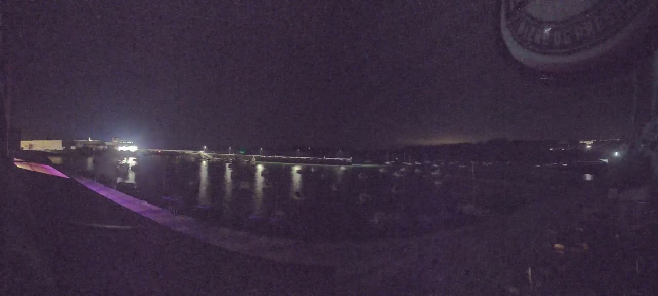 A nighttime view of a harbor filled with boats, illuminated by lights on the docks and buildings.