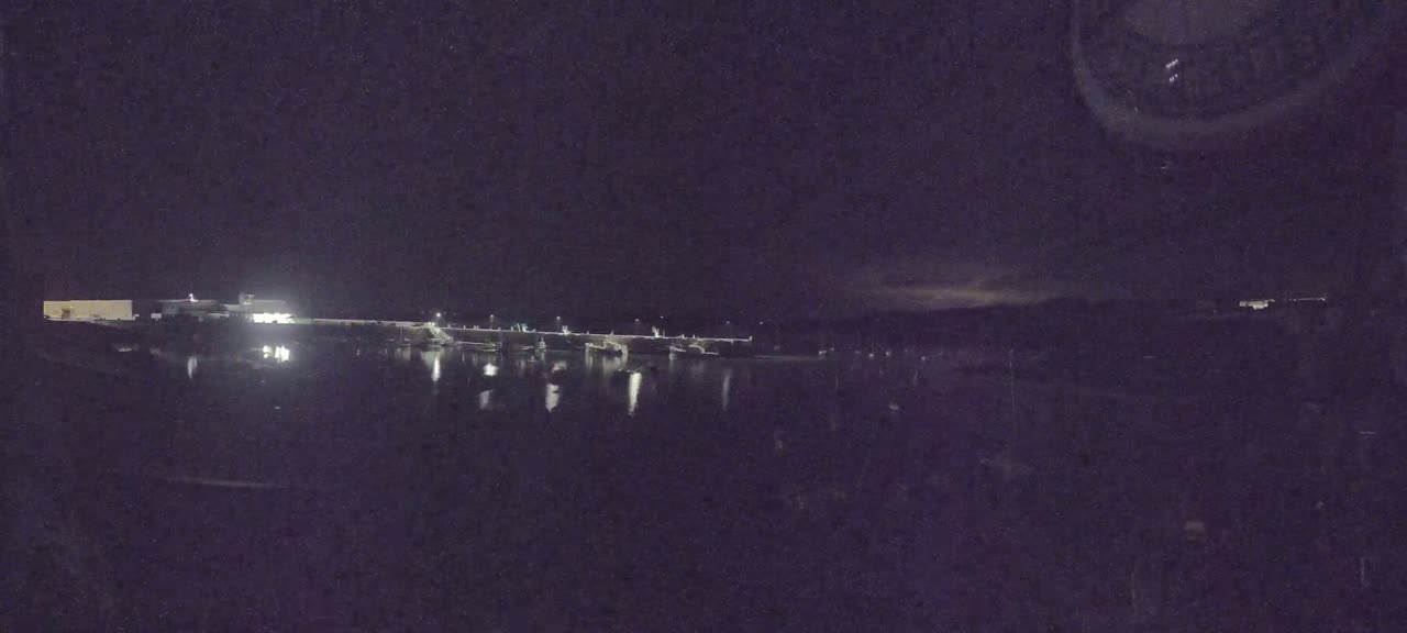 A nighttime view of a lit-up waterfront area with calm water reflecting the lights, under a dark sky.