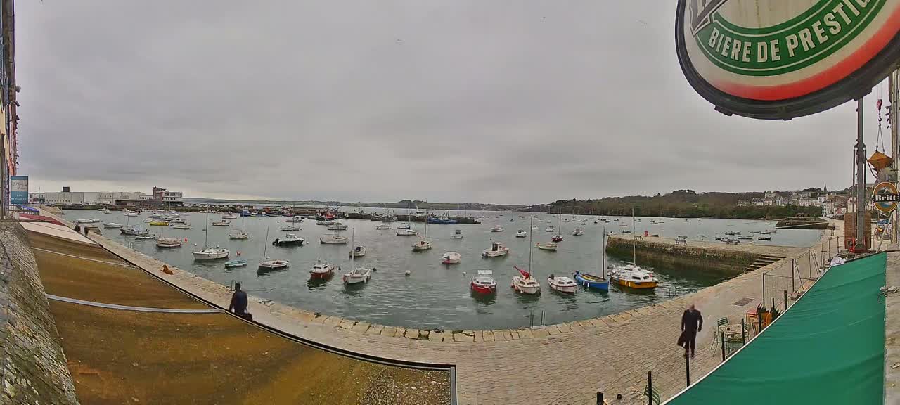 A harbor filled with numerous small boats is viewed from a quay on an overcast day.