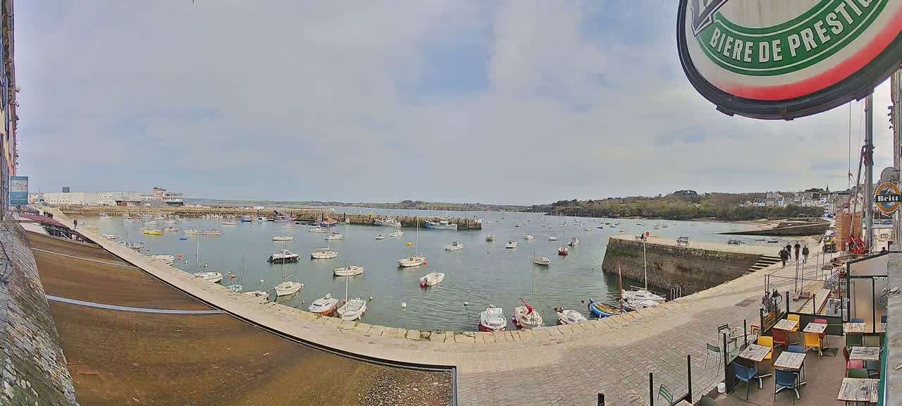 A harbor filled with numerous small boats under a partly cloudy sky, viewed from a waterfront patio.