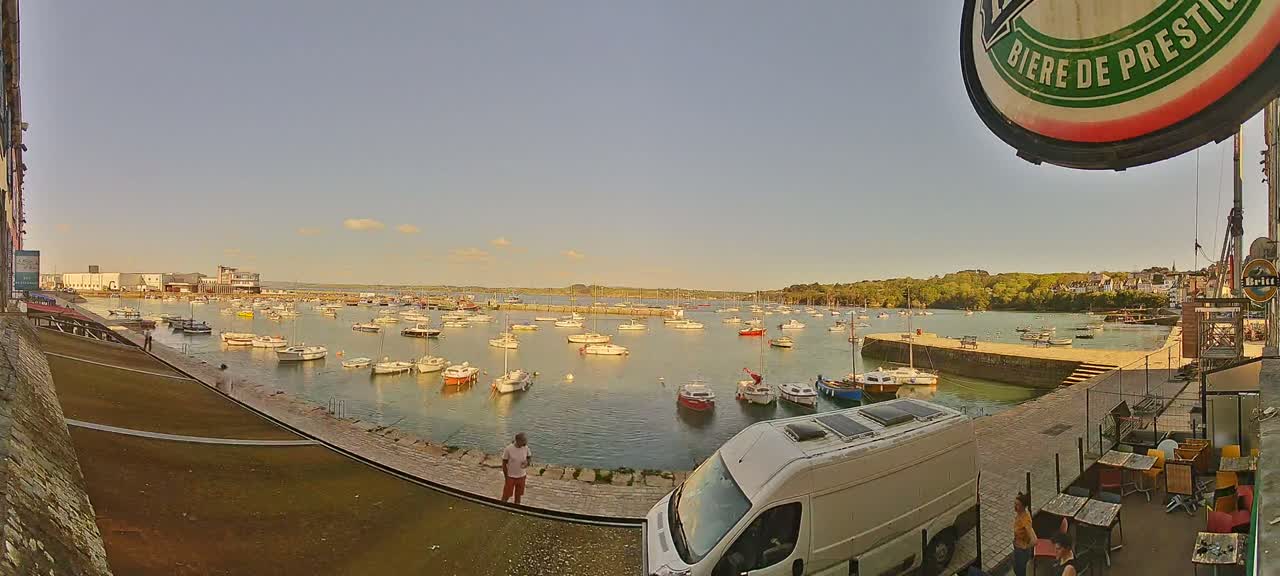 A calm harbor filled with numerous boats is viewed from a waterfront patio under a clear, sunny sky.