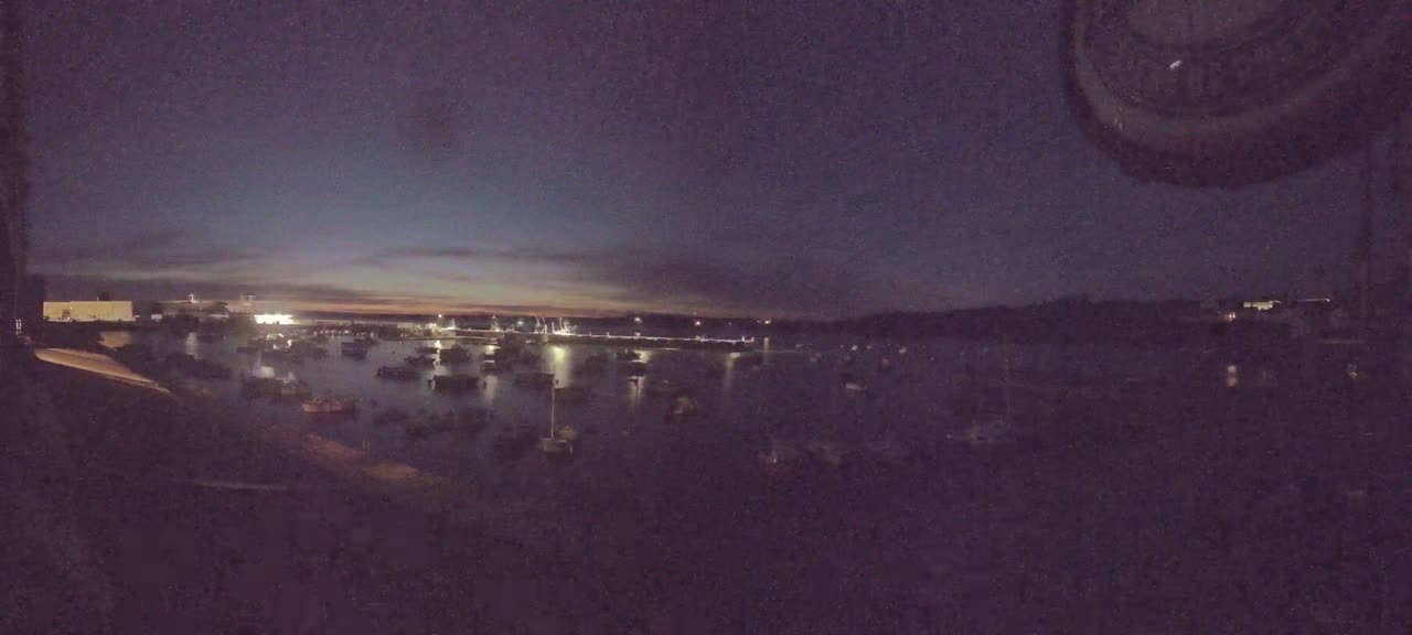 Many boats are moored in a dark harbor at twilight under a mostly clear sky.