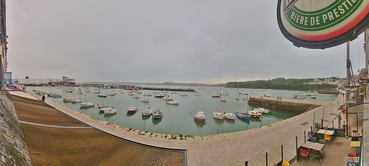 A harbor filled with numerous small sailboats and motorboats is viewed from a waterfront patio on an overcast day.