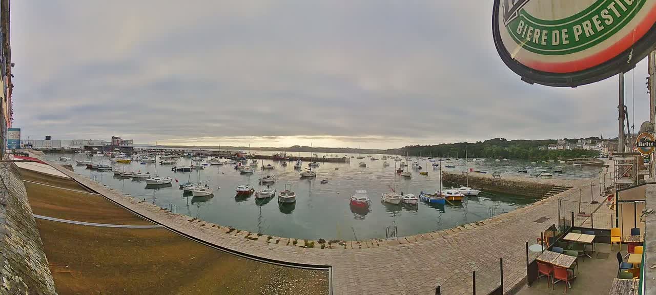 A harbor filled with numerous small boats under a cloudy sky, viewed from a patio area with outdoor seating.